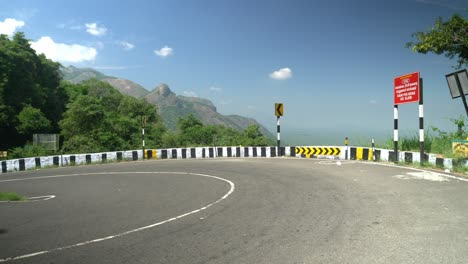 A-tourist-car-driving-through-a-winding-mountain-road-with-caution-signs-indicating-a-curve,-Hair-pin-bend-road-go-slow-red-sign-board