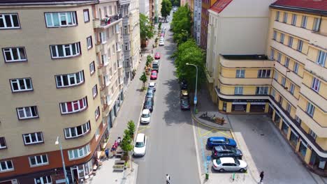 Flying-into-residential-street-in-Prague,-Czech-Republic,-lined-with-parked-cars-and-apartment-buildings