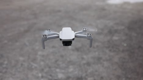 Small-grey-drone-hovers-flying-low-over-ground,-close-up-detail