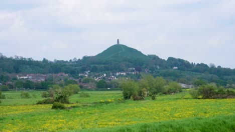 Vista-Panorámica-Del-Tor-En-La-Campiña-Rural-De-Glastonbury-Con-Vistas-A-Campos-Verdes-De-Flores-Amarillas-Silvestres-En-Los-Niveles-De-Somerset-En-Inglaterra