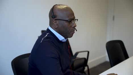 Bald-black-man-wearing-a-headset-while-working-in-an-office-meeting-room