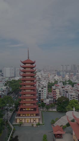 Vertical-video-of-Buddhist-Pagoda-in-Ho-Chi-Minh-City,-Vietnam-with-prayer-tower-and-red-roof-situated-in-densely-populated-area-of-the-city