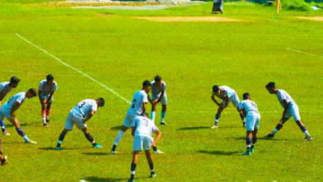 Hombres-Jóvenes-En-Un-Campo-De-Fútbol-En-Bangladesh,-Calentando-Con-Rigurosos-Estiramientos-Antes-Del-Partido-En-Medio-De-Un-Vibrante-Entorno-Verde.