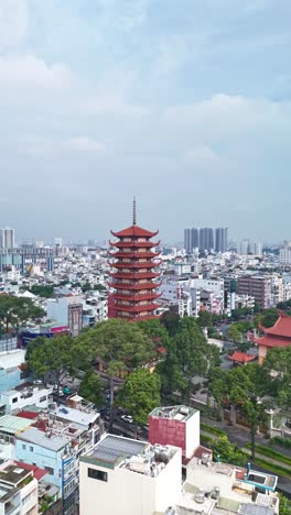 Vertical-hyperlapse-of-Buddhist-Pagoda-in-Ho-Chi-Minh-City,-Vietnam-with-prayer-tower-and-red-roof-situated-in-densely-populated-area-of-the-city