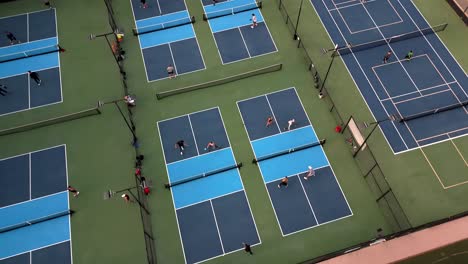 Pickleball-tournament-with-foursome-of-players,-aerial-ascending-over-multiple-courts