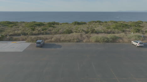 Aerial-perspective-of-a-coastal-California-scene,-featuring-a-parking-lot-situated-by-the-shoreline,-illustrating-the-concept-of-coastal-recreation-and-seaside-convenience