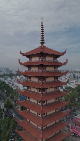 Vertical-video-of-Buddhist-Pagoda-in-Ho-Chi-Minh-City,-Vietnam-with-prayer-tower-and-red-roof-situated-in-densely-populated-area-of-the-city