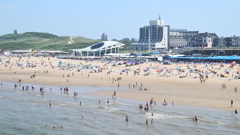 Sommerzeit-Am-Strand-Von-Scheveningen-Mit-Einheimischen-Und-Touristen,-Die-Im-Wasser-Der-Nordsee-Schwimmen