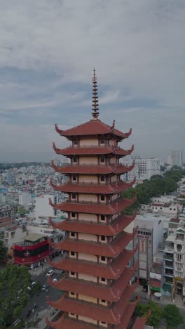 Vertical-video-of-Buddhist-Pagoda-in-Ho-Chi-Minh-City,-Vietnam-with-prayer-tower-and-red-roof-situated-in-densely-populated-area-of-the-city