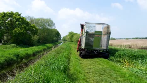 Close-up-of-grass-cutter-machine-driving-alongside-river-in-nature-reserve-on-the-Somerset-Levels-in-England-UK