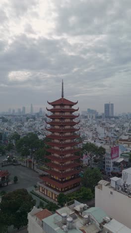 Vertical-video-of-Buddhist-Pagoda-in-Ho-Chi-Minh-City,-Vietnam-with-prayer-tower-and-red-roof-situated-in-densely-populated-area-of-the-city