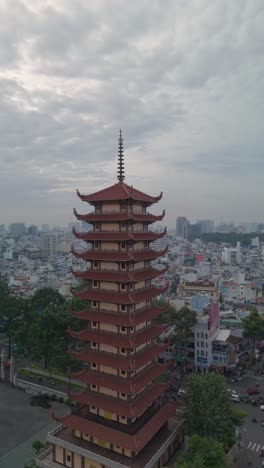 Vertical-video-of-Buddhist-Pagoda-in-Ho-Chi-Minh-City,-Vietnam-with-prayer-tower-and-red-roof-situated-in-densely-populated-area-of-the-city