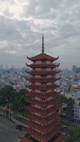 Vertical-video-of-Buddhist-Pagoda-in-Ho-Chi-Minh-City,-Vietnam-with-prayer-tower-and-red-roof-situated-in-densely-populated-area-of-the-city