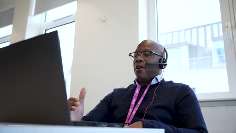 Schwarzer-Männlicher-Berufstätiger-Mit-Brille-Und-Headset,-Der-In-Einem-Modernen-Konferenzraum-An-Einem-Laptop-Arbeitet