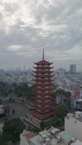 Vertical-video-of-Buddhist-Pagoda-in-Ho-Chi-Minh-City,-Vietnam-with-prayer-tower-and-red-roof-situated-in-densely-populated-area-of-the-city