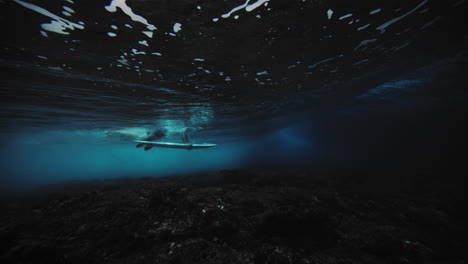 Underwater-angle-sideview-of-surfer-duck-diving-and-pushing-down-on-board-as-wave-crashes