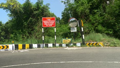 A-tourist-car-driving-through-a-winding-mountain-road-with-caution-signs-indicating-a-curve,-Hair-pin-bend-road-go-slow-red-signboard-and-traffic-mirror