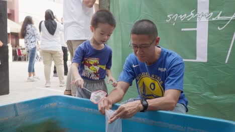 Un-Niño-Pescando-Con-La-Ayuda-De-Su-Padre-En-Un-Festival-Al-Aire-Libre,-Yakarta-Barat,-Indonesia