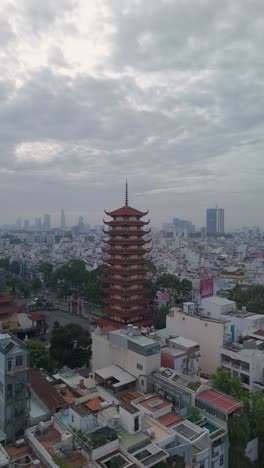 Vertical-video-of-Buddhist-Pagoda-in-Ho-Chi-Minh-City,-Vietnam-with-prayer-tower-and-red-roof-situated-in-densely-populated-area-of-the-city