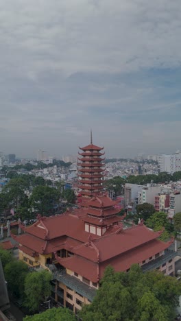 Vertical-video-of-Buddhist-Pagoda-in-Ho-Chi-Minh-City,-Vietnam-with-prayer-tower-and-red-roof-situated-in-densely-populated-area-of-the-city