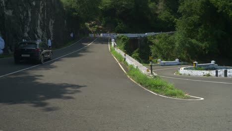 A-tourist-car-driving-through-a-winding-mountain-road-with-caution-signs-indicating-a-curve,-Hair-pin-bend-road-go-slow-red-sign-board