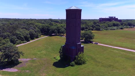 An-aerial-view-of-a-tall-brick-water-tower-on-a-sunny-day-in-a-large-green-field-on-the-Pilgrim-Psychiatric-Center-on-Long-Island,-NY