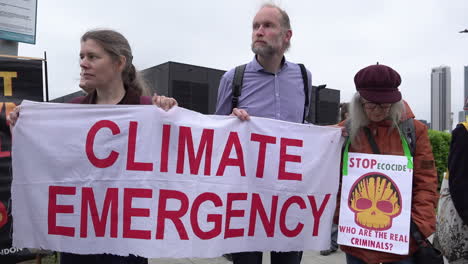Protestors-hold-a-banner-that-reads-in-red-writing,-“Climate-emergency”-as-a-third-person-holds-a-placard-depicting-the-Shell-Oil-and-Gas-logo-and-reads,-“Stop-ecocide
