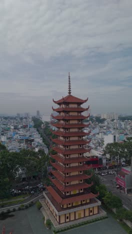 Vertical-video-of-Buddhist-Pagoda-in-Ho-Chi-Minh-City,-Vietnam-with-prayer-tower-and-red-roof-situated-in-densely-populated-area-of-the-city