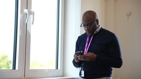 Black-Businessman-with-an-ID-card-lanyard-around-his-neck-is-talking-on-a-phone-near-a-window-in-a-bright-room,-symbolizing-communication-and-professionalism-in-a-workplace-setting