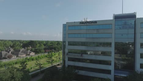 An-aerial-drone-view-of-a-work-crew-pressure-washing-a-high-rise-office-building-from-a-suspended-scaffold-in-Clear-Lake,-Houston,-Texas