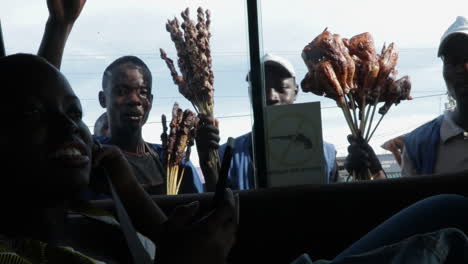 black-african-young-vendor-selling-skewers-of-meat-at-road-intersection,-view-from-inside-a-bus-public-transportation