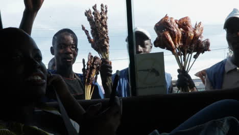 Joven-Vendedor-Negro-Africano-Vendiendo-Brochetas-De-Carne-En-La-Intersección-De-Carreteras,-Vista-Desde-El-Interior-De-Un-Autobús-De-Transporte-Público