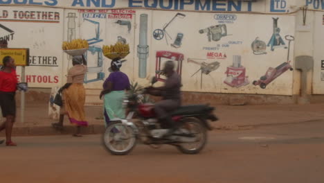 Two-African-Women-Carrying-Bananas-On-Their-Head-While-Crossing-Road-In-Uganda,-Africa