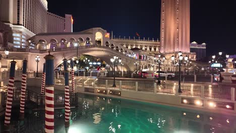 Kanal-Und-Brücke-Im-Venezianischen-Stil-Mit-Gestreiften-Masten-Und-Beleuchtetem-Wasser-Bei-Nacht-In-Las-Vegas