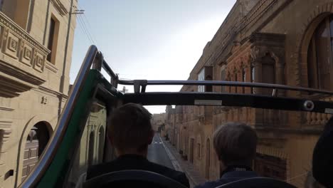 Los-Viajeros-Disfrutan-De-Un-Paseo-En-El-Piso-Superior-Abierto-De-Un-Autobús-Turístico-Por-Las-Pequeñas-Y-Estrechas-Calles-De-Gozo,-Malta,-Capturando-El-Encanto-Y-La-Exploración-íntima-De-La-Vida-Isleña.