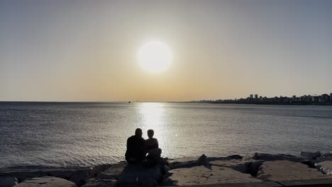 Happy-couple-sitting-on-the-beach-at-sunset