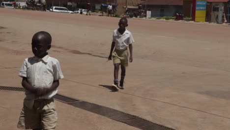 Two-boys-in-school-uniforms-walking-on-a-sunny-street-in-Kampala,-Uganda