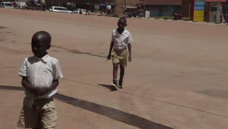 Dos-Niños-Con-Uniformes-Escolares-Caminando-Por-Una-Calle-Soleada-En-Kampala,-Uganda