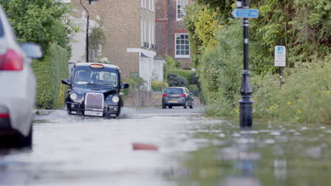 Black-taxi-drives-along-a-very-flooded-road-in-London,-telephoto