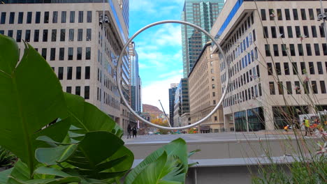 Urban-Circular-Sculpture-Surrounded-By-Buildings-In-Downtown-Montreal-City,-Tracking-Sideways-View