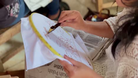 A-woman's-hands-with-white-skin-are-using-a-"canting"-tool-to-draw-batik-patterns-on-white-cloth