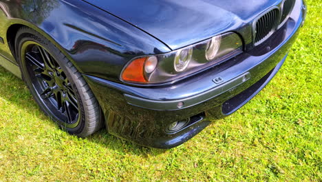 Shiny-hood,-tire,-and-front-end-of-a-BMW-M5-E39-automobile-parked-on-grass---isolated