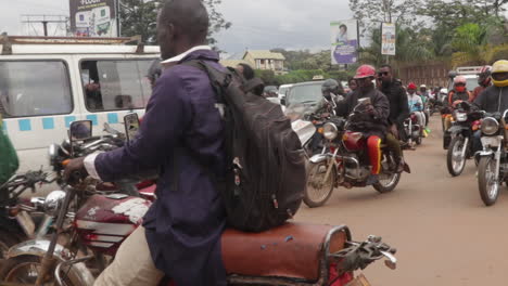 Motorcycles-and-a-white-van-crossing-a-busy-street-during-rush-hour-in-Kampala,-Uganda,-under-a-cloudy-sky