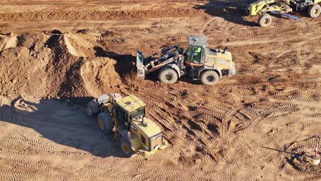 Luftaufnahme-Von-Zwei-Frontladern,-Die-Ihre-Schaufeln-Auf-Einer-Neuen-Wohnbaustelle-Füllen