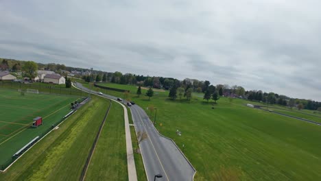 FPV-Flight-over-intersection-with-driving-cars-near-american-school-and-sport-field