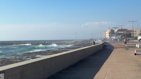 Strong-waves-crashed-onto-the-walkway,-and-a-boy-kicked-a-ball-in-Praia-do-Furadouro,-Ovar,-Portugal