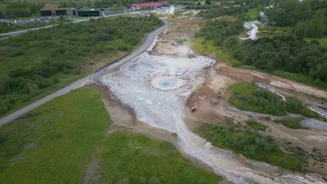 Geyser-erupts-in-a-vast-green-landscape,-aerial-view,-Iceland