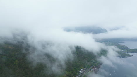 Vuelo-Aéreo-A-Través-De-Nubes-Sobre-Edificios-Y-Carreteras-En-La-Costa-De-Glen-Coe,-Escocia