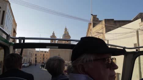 Tourists-savor-an-open-air-journey-on-the-upper-deck-of-a-sightseeing-bus-through-the-quaint-and-narrow-lanes-of-Gozo,-Malta,-immersing-themselves-in-the-island’s-charm-and-intimate-exploration