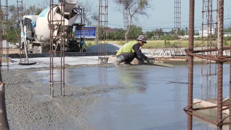 Einsamer-Bauarbeiter-Nivelliert-Die-Frisch-Gegossene-Zementmischung-Auf-Dem-Boden-Eines-Im-Bau-Befindlichen-Gebäudes-Am-Stadtrand-Von-Bangkok,-Thailand